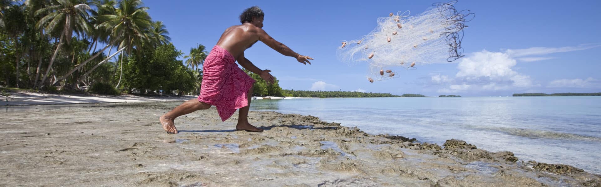 A fisherman on the coast of Funafui, Tuvalu, throwing a weighted net out into the sea water, a traditional form of fishing.